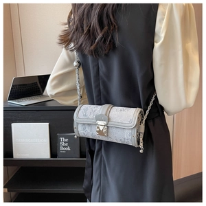 Detail of grey cylindrical chain bag featuring embossed textures and metal M clasp