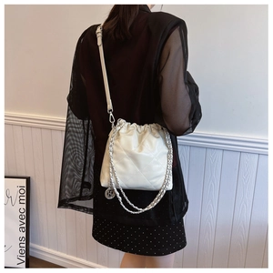 Detail view of cream quilted bucket bag with silver chain and HD brand charm