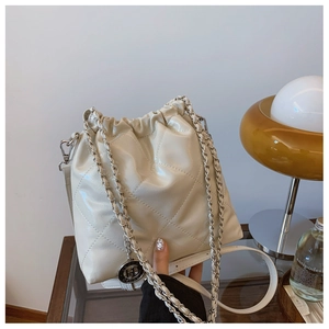 Detail of quilted beige bucket bag with metal chain strap on reflective glass table