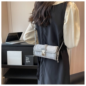 Detail of grey chain crossbody bag with M-logo buckle shown in a modern office setting