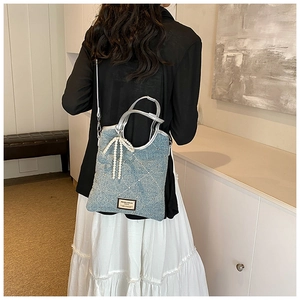 Détail du sac en jean bleu clair avec nœud en perles et surpiqûres en strass