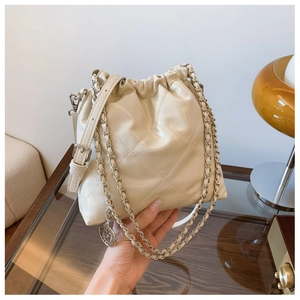 Close-up of beige quilted bucket bag with gold chain strap and drawstring closure