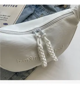 Détail du sac croissant blanc en nylon avec broderie et double fermeture éclair sur denim