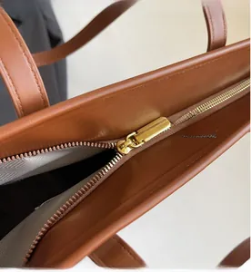 Detail of smooth gold zipper and herringbone fabric lining on brown leather tote bag