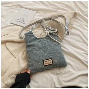Détail d'un sac à main en denim gris matelassé avec strass et pendentif nœud en perle