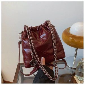 Detail of burgundy quilted bucket bag with gold chain strap and metallic logo charm