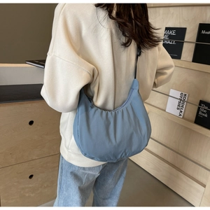 Morandi blue nylon dumpling bag shown as a shoulder bag on a model in a cozy library