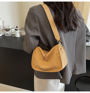 Detail shot of woven crescent bag featuring a wide leather strap and golden hardware