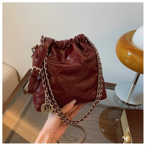 Detail of burgundy quilted bucket bag with chain strap and round metallic logo charm