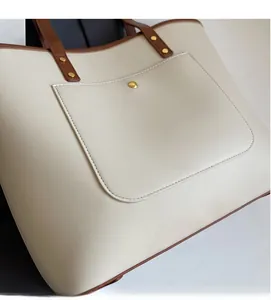 Detail of cream tote bag featuring brown trim and gold rivet pocket accents