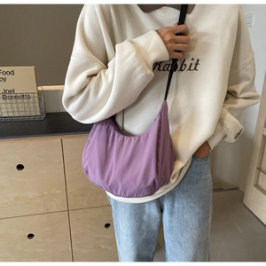 Detail of a purple nylon crescent bag worn by a model in a cozy minimalist interior