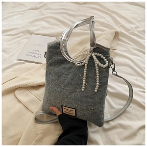 Détail du sac en jean gris avec coutures en losange, clous argentés et charm nœud perlé