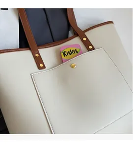 Detail view of the large front pocket on this cream tote bag with brown trim and gold buckle