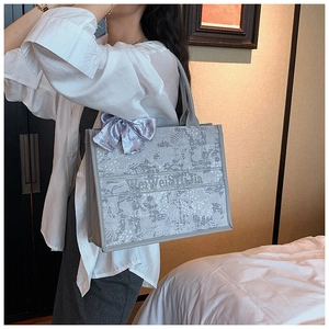 Détail du sac cabas en toile brodée grise avec un nœud en soie décoratif sur l'anse