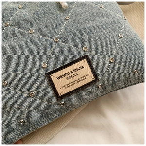 Détail du sac à bandoulière en jean bleu clair avec motif losange et rivets argentés