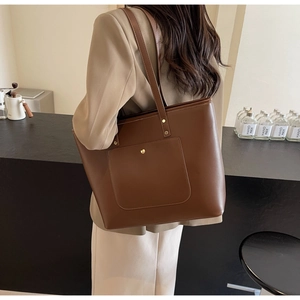 Close-up of a brown leather tote bag showing the front pocket with gold rivet detail