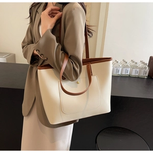 Close-up of beige tote bag with brown trim and gold stud detail on a female model