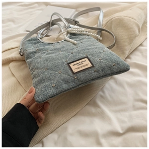 Détail du sac en jean bleu clair avec motif matelassé, rivets et poignée en perles