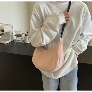 Pale pink nylon crescent bag shown worn cross-body in a cozy modern cafe setting
