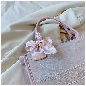 Détail du sac cabas rose clair avec broderie florale et grand nœud en soie sur l'anse
