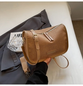 Close-up of woven straw handbag with dual zipper details and adjustable shoulder strap