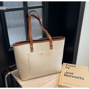 Detail of minimalist tote bag with cream leather, brown straps, and gold button snap pocket