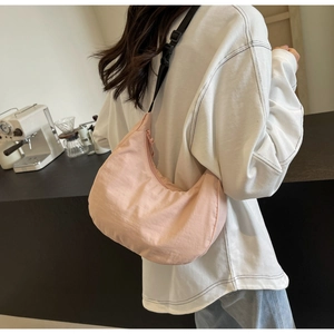 Detail of light pink nylon hobo bag with adjustable black strap worn by a model