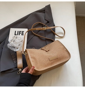 Detail of woven straw shoulder bag featuring adjustable leather strap and brand logo plate