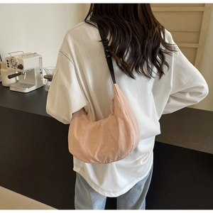 Rear view of a pink nylon crescent bag worn on a shoulder in a minimalist cafe
