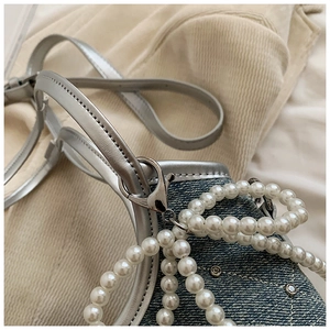 Détail du sac en denim bleu avec garniture en cuir argenté, perles et strass brillants