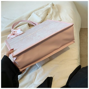 Détail d'un sac cabas rose clair avec motifs discrets et nœud en soie sur l'anse