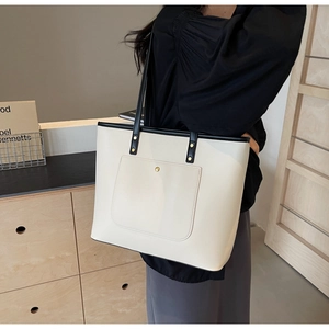 Detail of cream tote bag with contrast black handles and front gold button pocket