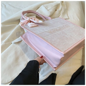 Détail d'un cabas rose brodé avec un ruban élégant et des panneaux en cuir souple