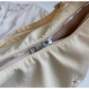 Dettaglio borsa in nylon crema con cerniera argentata e ricamo a stella dorata sul lato