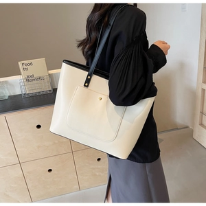 Detail of cream tote bag with black trim, magnetic buckle pocket, and gold hardware rivets