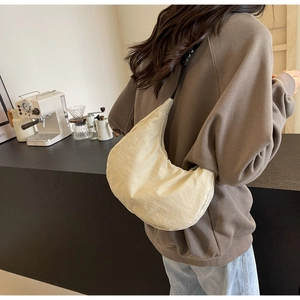 Detail of off-white crescent nylon bag with adjustable black strap on model