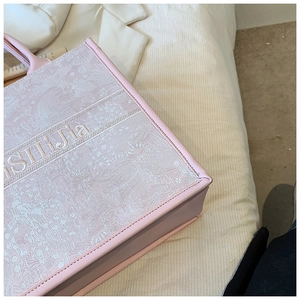 Détail d'un sac cabas rose clair avec broderie florale et lettrage sur un tissu texturé