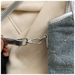 Détail du sac en jean bleu clair avec garniture en cuir argenté et clous en strass sur fond doux