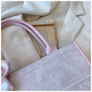 Détail du sac cabas jacquard rose pâle avec nœud en satin sur un fond de veste blanche