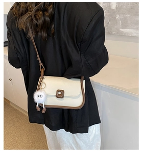 Close-up of minimalist bicolor crossbody bag with plush charm and contrast piping