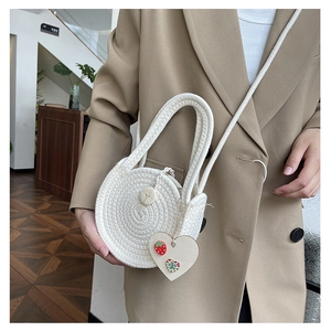 Detail of round straw bag with heart pendant and woven handles shown with lifestyle outfit