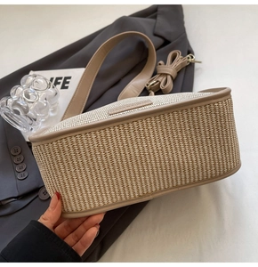 Detail of beige woven straw bag featuring brown faux leather trim and dual strap design