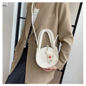Detailed close-up of a white woven round crossbody bag with a heart pendant