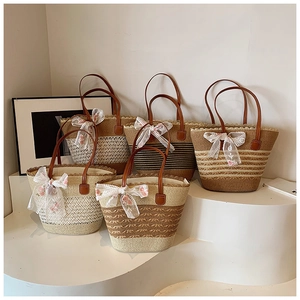 Detail of five woven straw tote bags with brown PU handles and lace bow decorations