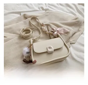 Detail of cream crossbody bag featuring silk scarf strap and plush monster charm