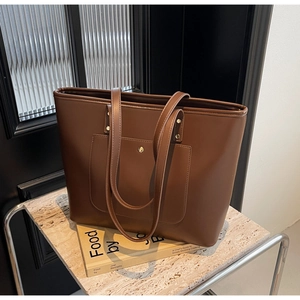Detail of a large brown faux leather tote bag showing the exterior pocket and golden buckle