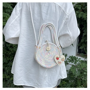 Detail of white round woven straw bag with colorful stitching and heart-shaped charm