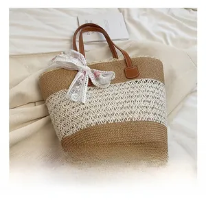 Detail of khaki straw tote bag with white lace bow and brown leather handles