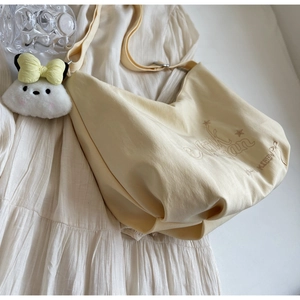 Dettaglio borsa a tracolla in tela beige con ricami marroni e ciondolo a forma di coniglio
