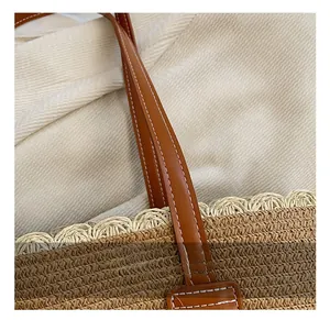 Detail of woven straw tote bag featuring brown leather handle with white contrast stitching